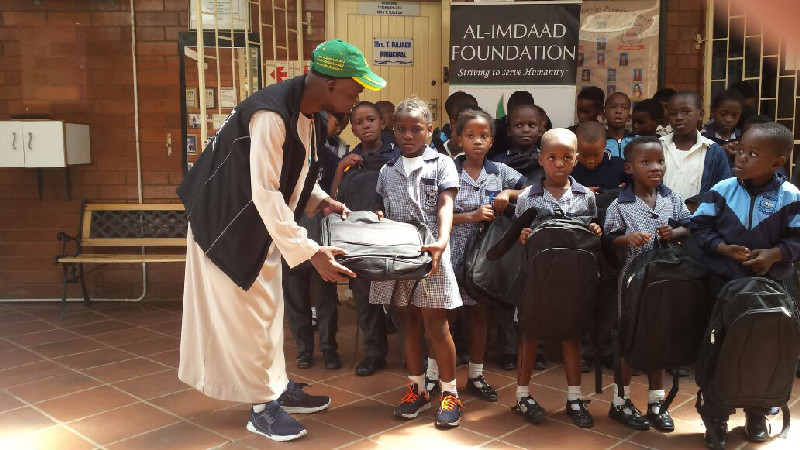 An Al-Imdaad Foundation representative hands over a bag to a young beneficiary 